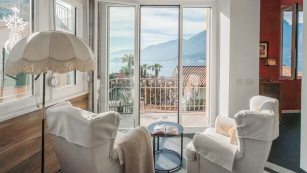 A room with a balcony, white chairs, a round table, and a floor lamp. - Villa Casa Pini (Bellagio)