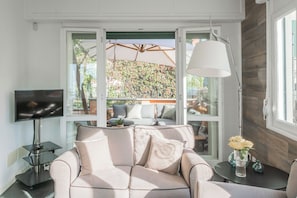 Una sala de estar con un sofá, televisor y una mesa con un jarrón de flores.