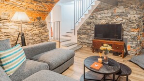 A living room with a stone wall, a sofa, a coffee table, a lamp, and a TV. - Villa Casa Pini (Bellagio)