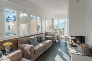 A living room with a sofa, a fireplace, and a view of the outdoors. - Villa Casa Pini (Bellagio)