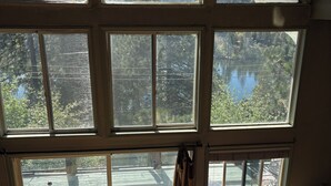Une pièce dotée de grandes fenêtres, d’une terrasse en bois et d’un canapé marron agrémenté de coussins.
