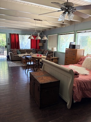 A spacious living room with a ceiling fan, a dining table, a sofa, a bed, and a wooden dresser.