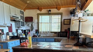 Une cuisine avec un plafond en bois, un îlot central doté de tabourets et une fenêtre avec des stores.