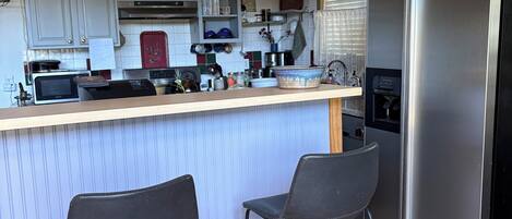 Une cuisine avec un plafond en bois, un réfrigérateur en acier inoxydable, deux tabourets de bar et un four à micro-ondes.