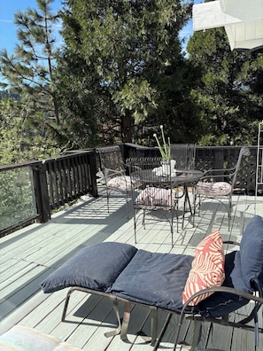 A deck with outdoor furniture, including a lounge chair and a table with chairs, surrounded by a wooden railing.