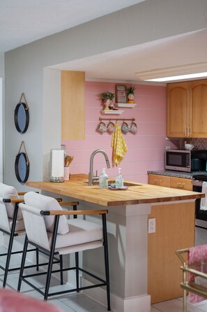 A kitchen with a central island, bar stools, a microwave, and wooden cabinets. - Walk to Beach | Cowboy Pool | Sleeps 6 | Pets OK (St. Augustine)