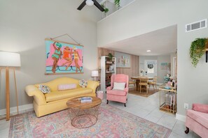 Una sala de estar con un sofá amarillo, un sillón rosa, una mesa de centro y una alfombra colorida.