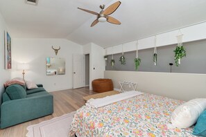 Un dormitorio con cama, sofá verde, ventilador de techo, exposición de plantas en la pared y un espejo.