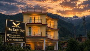 Un hotel de varios pisos con balcones, un letrero y montañas al fondo.