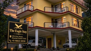 Un hotel de varios pisos con balcones, un cartel y automóviles estacionados.