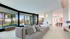 Un salon moderne doté d’un grand canapé d’angle, d’un coin repas et offrant une vue sur une piscine et un espace verdoyant.