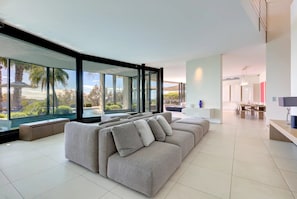 Ein modernes Wohnzimmer mit einem großen Ecksofa, einem Essbereich und Blick auf einen Pool und Grünflächen.