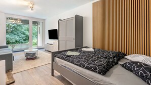 Ein modernes Schlafzimmer mit Bett, Fernseher, Kleiderschrank und Blick ins Grüne.