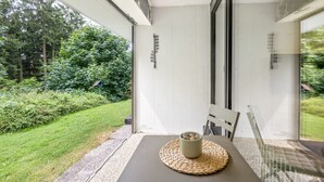 Ein Zimmer mit Tisch, Stuhl, Fenster und Blick auf Grünfläche.