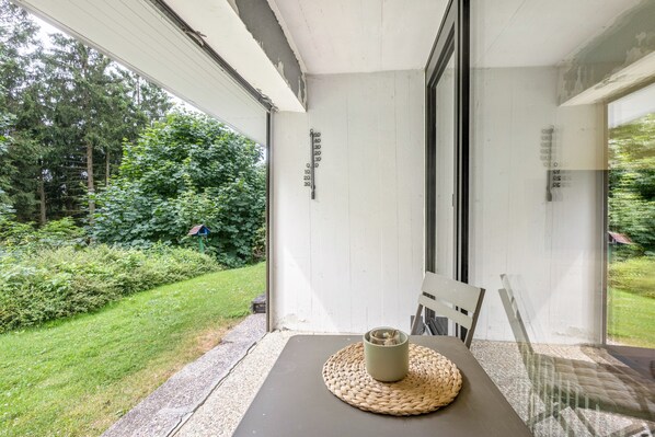 A room with a table, a chair, a window, and a view of greenery.
