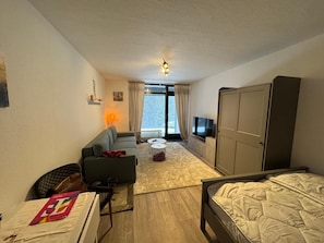 Quarto de hotel com sofá, cama, televisão, escrivaninha, cadeira, mesa pequena e guarda-roupa.