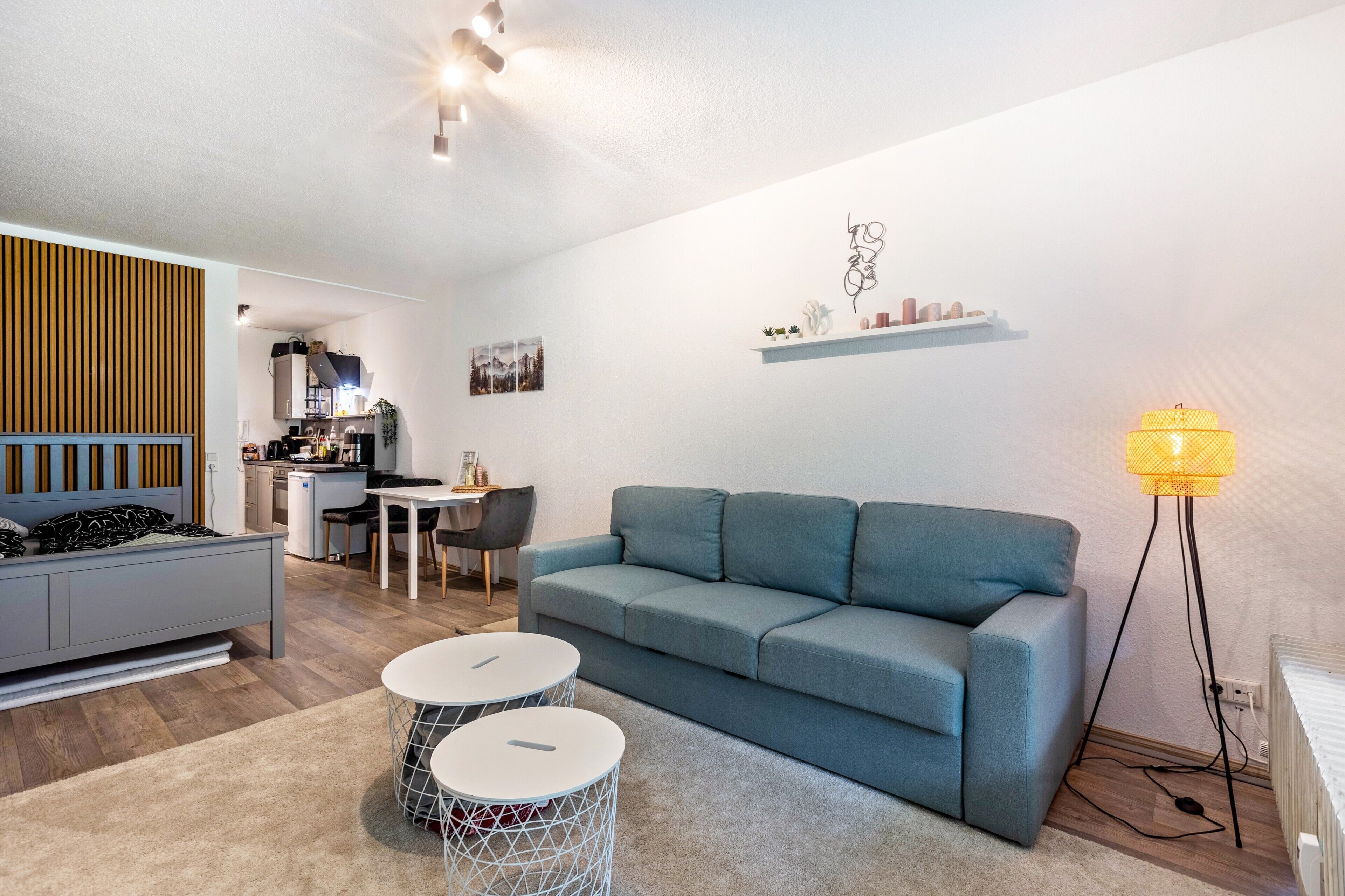 A modern living room with a grey sofa, two round tables, a kitchen in the background, and a floor lamp.