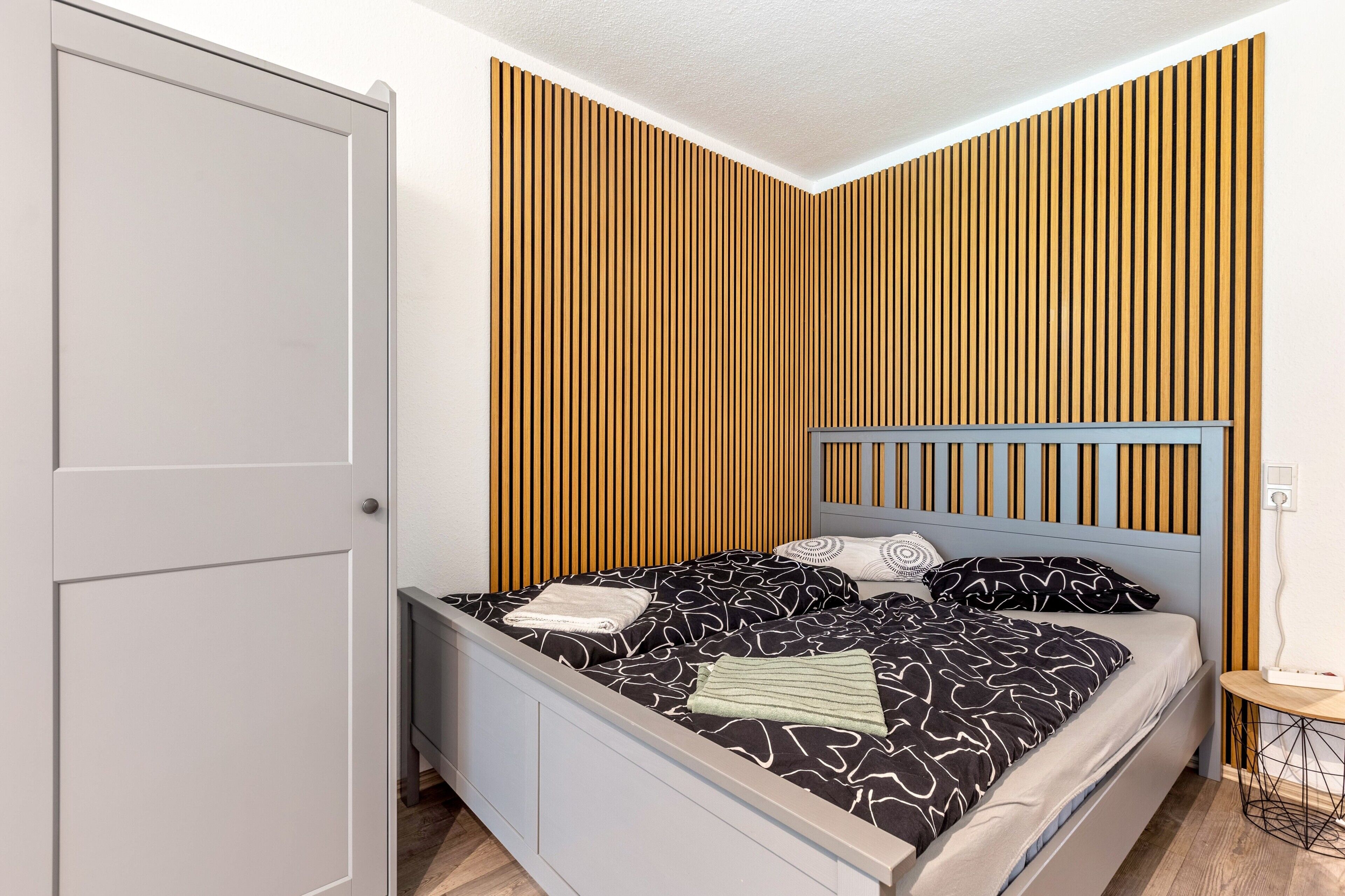 Une chambre à coucher comprenant un lit, une table de chevet, un mur avec des lambris en bois verticaux et une porte.