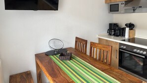 A kitchen with a wooden table, chairs, a TV, a microwave, a coffee maker, and an oven. - Apartment 'Meerestraum' with Wi-Fi (Norden)