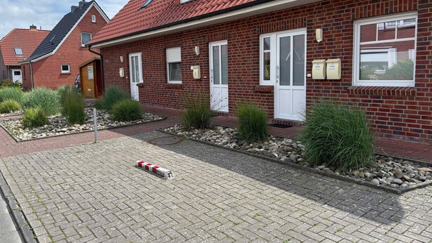 A red-brick building with white-framed windows and doors, a paved driveway, and a small garden area with plants. - Apartment 'Meerestraum' with Wi-Fi (Norden)
