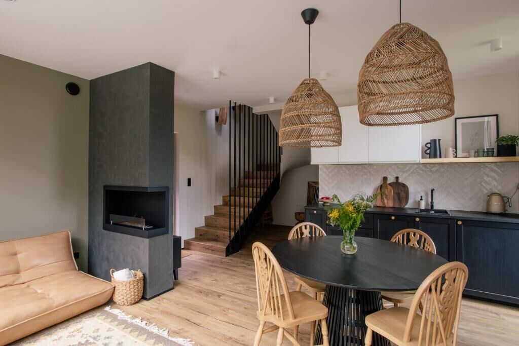 A modern living room with a sofa, dining table, and chairs, a fireplace, and a kitchen area with a staircase.