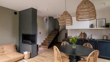 A modern living room with a sofa, dining table, and chairs, a fireplace, and a kitchen area with a staircase.