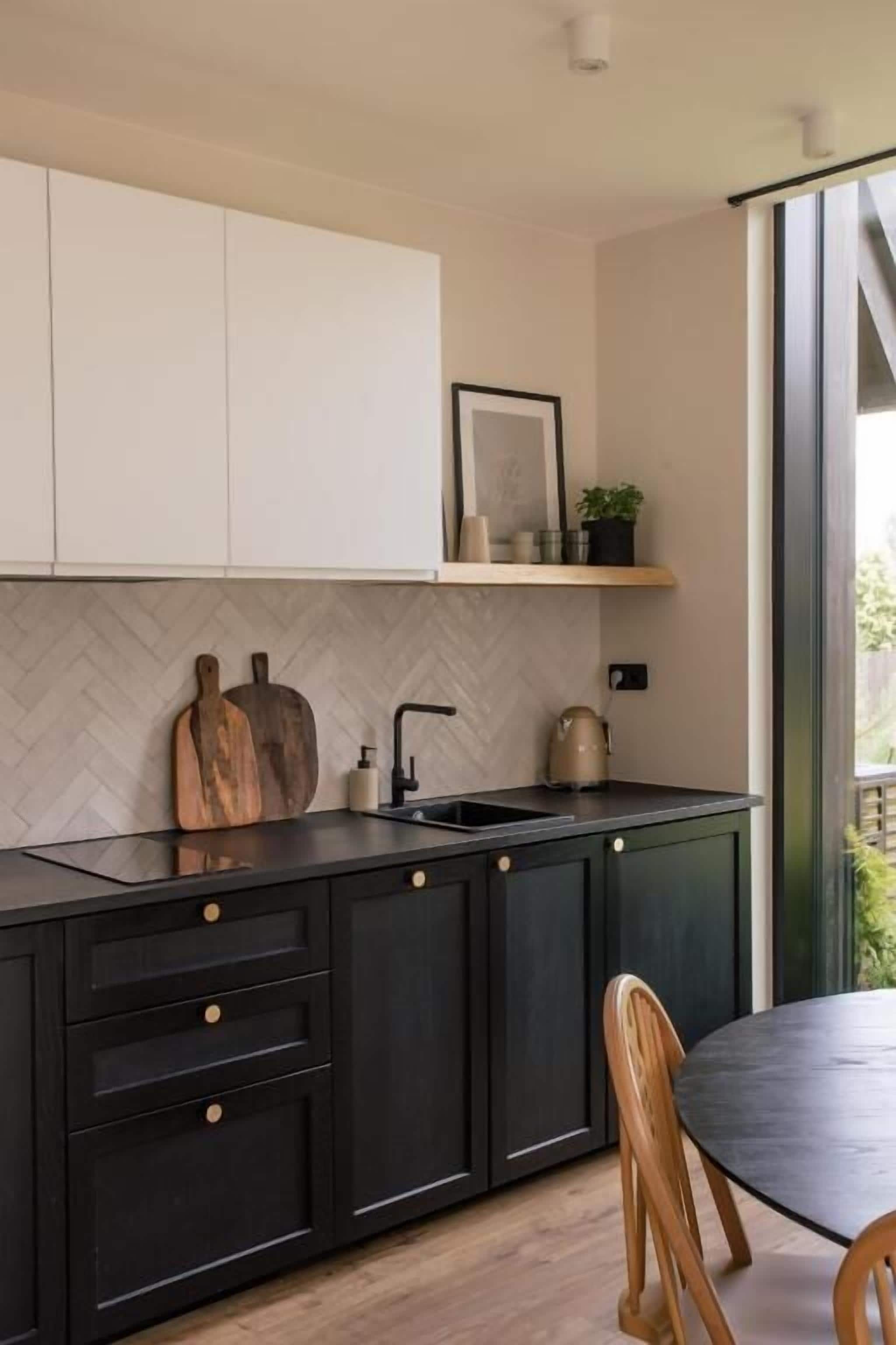 Una cocina moderna con armarios negros, un salpicadero tipo espiga y una tabla de cortar de madera.