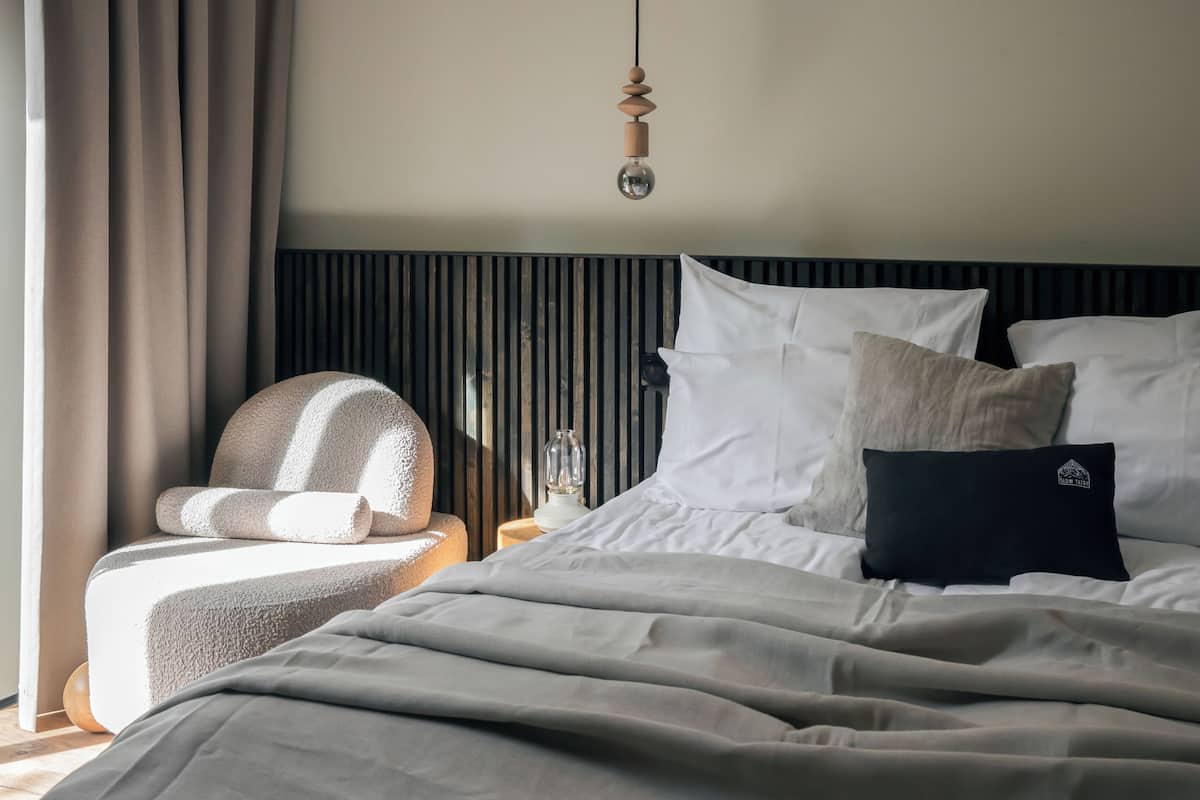 A neatly made bed with white and black pillows, a bedside lamp, and a modern chair.