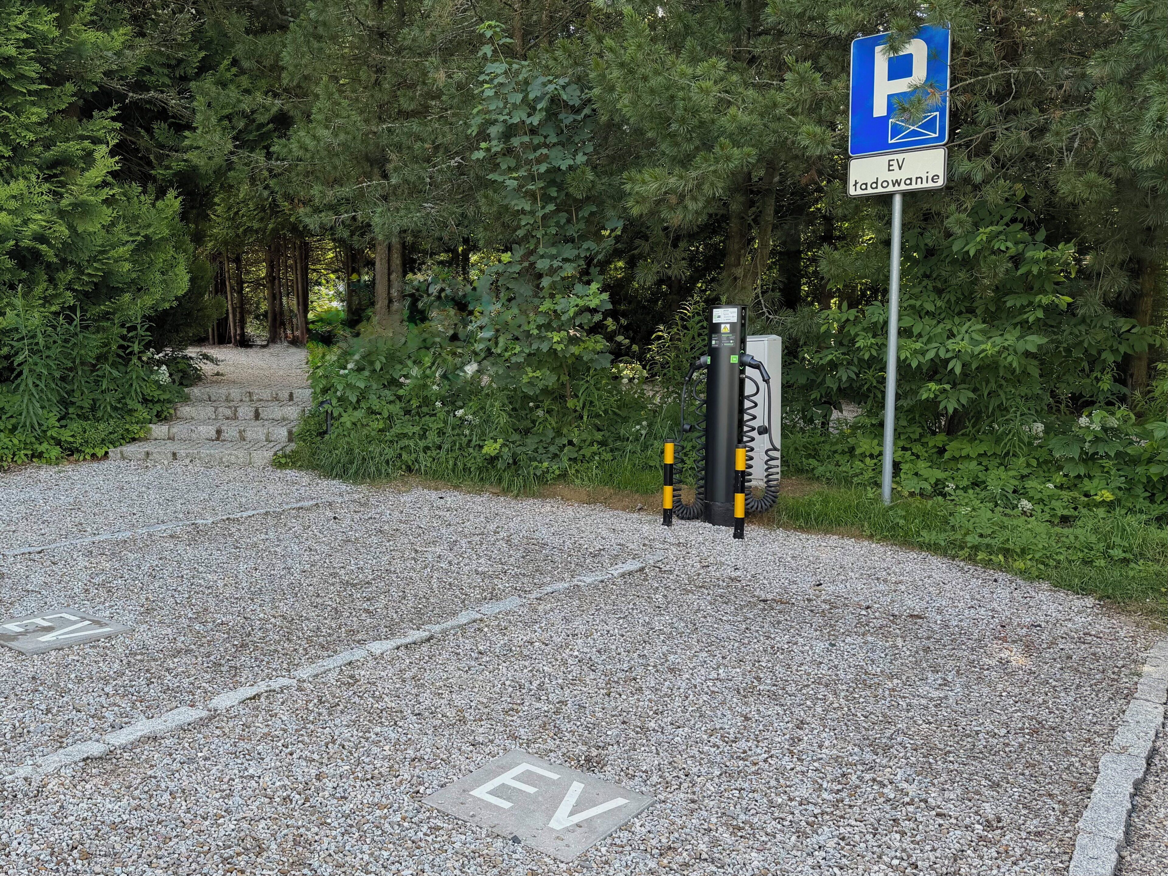 A gravel parking area with EV charging stations and a blue parking sign.