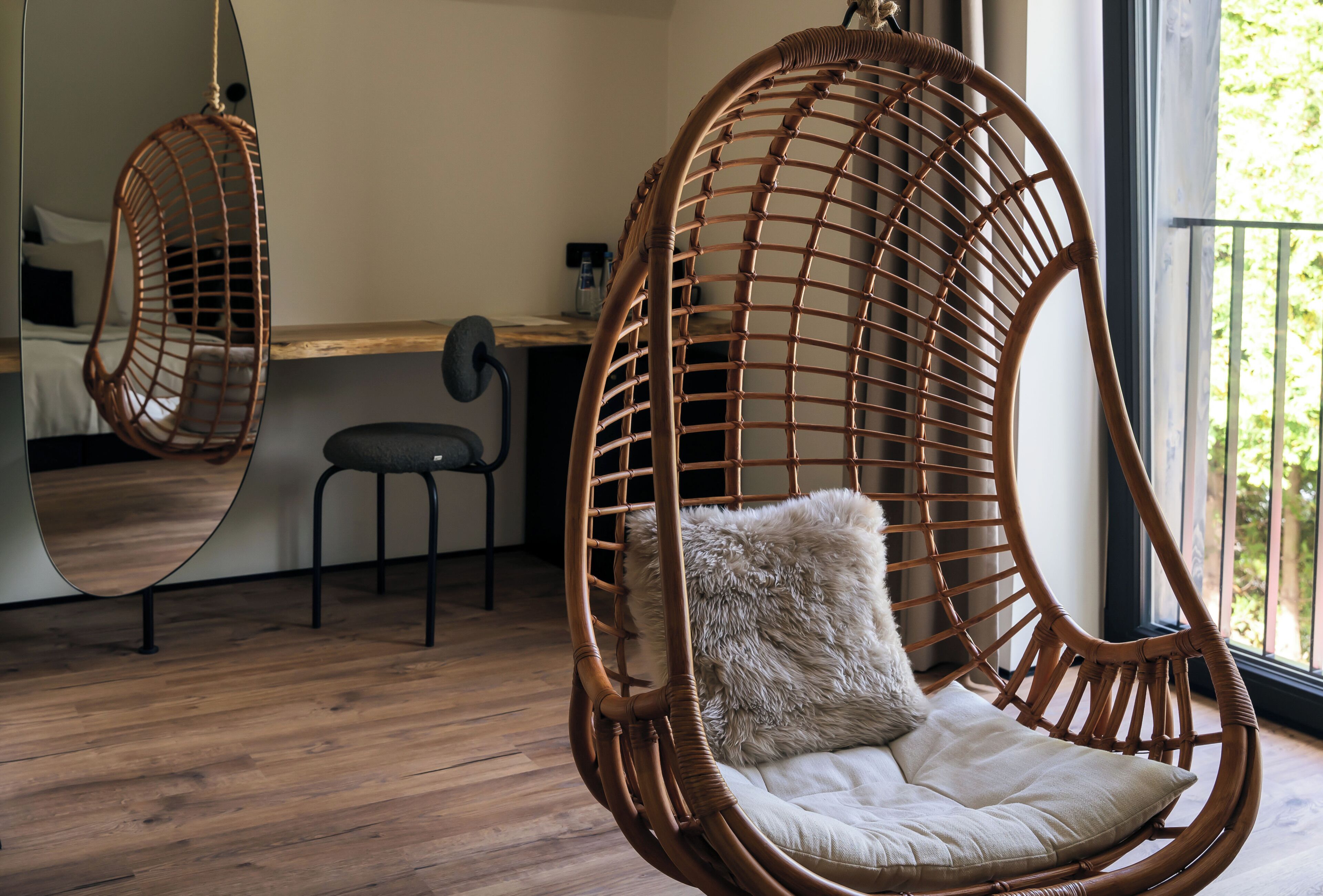Une pièce avec un fauteuil suspendu, une petite table et un miroir qui reflète l’intérieur.