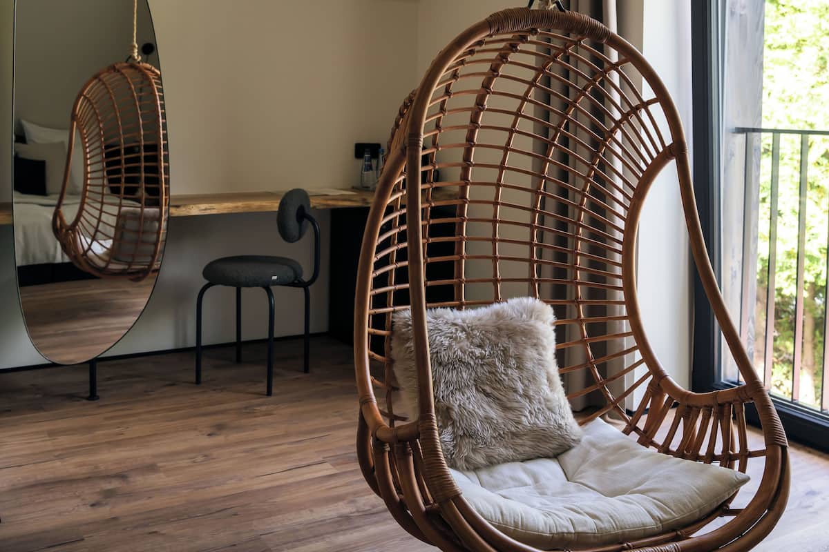 A room with a hanging chair, a small table, and a mirror reflecting the room.