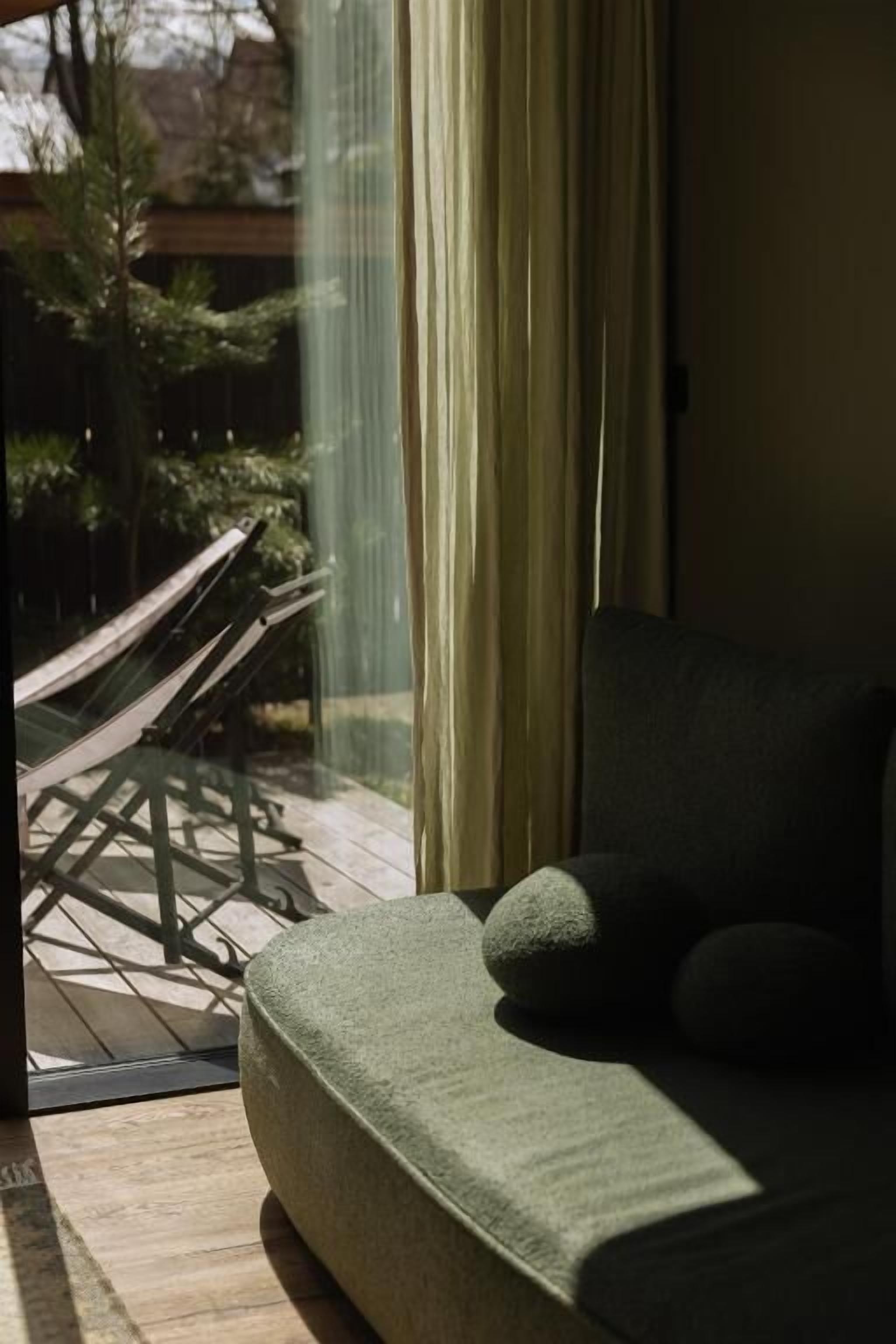 Una habitación con sofá, ventana con cortinas y vistas a una terraza de madera con hamaca.