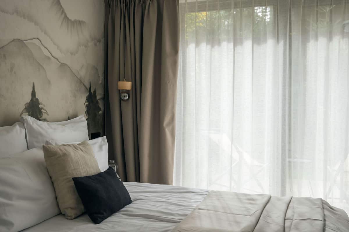 A bed with white bedding, a dark pillow, and a wall with a mountain painting.