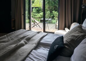 Une chambre Ă coucher avec un lit, un oreiller et une vue sur une terrasse et un jardin, grĂące Ă de grandes fenĂȘtres.