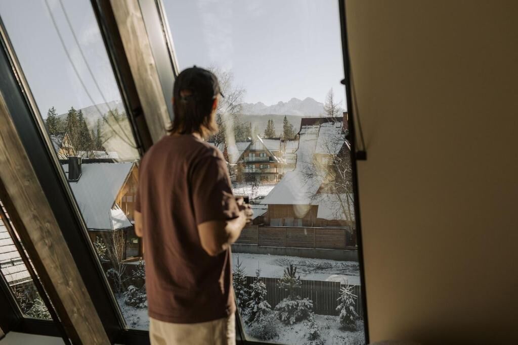 Een persoon staat bij een raam met uitzicht op een besneeerd landschap en een skilift.