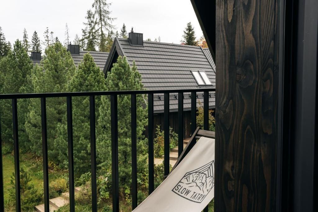 A balcony with a metal railing, a view of a house with a sloped roof, and a sign with the text 'SLOW TATRY.'