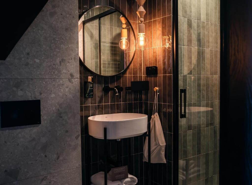 A modern bathroom with a round mirror, a white sink, and a glass shower enclosure.
