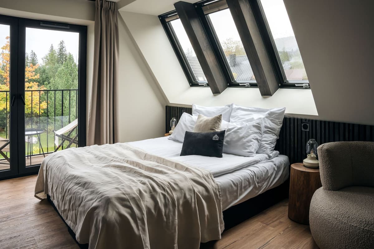 A bedroom with a sloped ceiling, a bed with white bedding, a nightstand, and a chair.