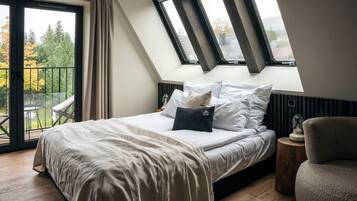 A bedroom with a sloped ceiling, a bed with white bedding, a nightstand, and a chair.
