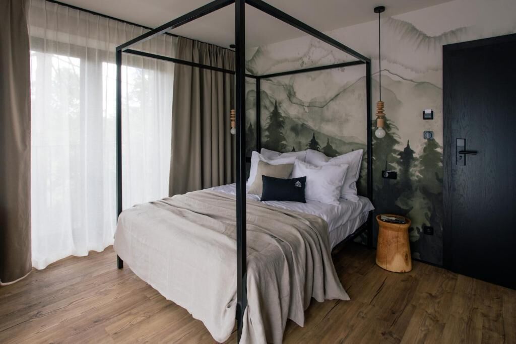 A four-poster bed with a mountain mural, a wooden floor, a wooden stool, and a dark door.