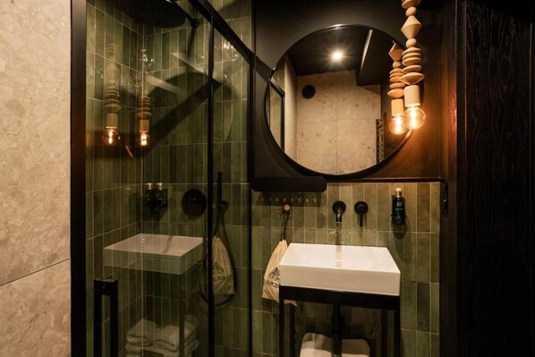 Une salle de bain moderne avec une douche Ă parois de verre, deux vasques, un miroir rond et un luminaire en bois.