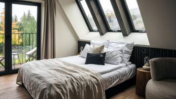 A bedroom with a large bed, a skylight, a balcony, and a view of trees.