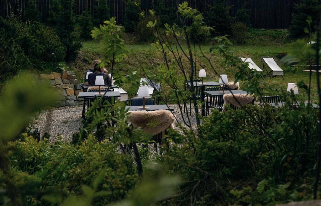 An outdoor seating area with tables and chairs, surrounded by greenery.
