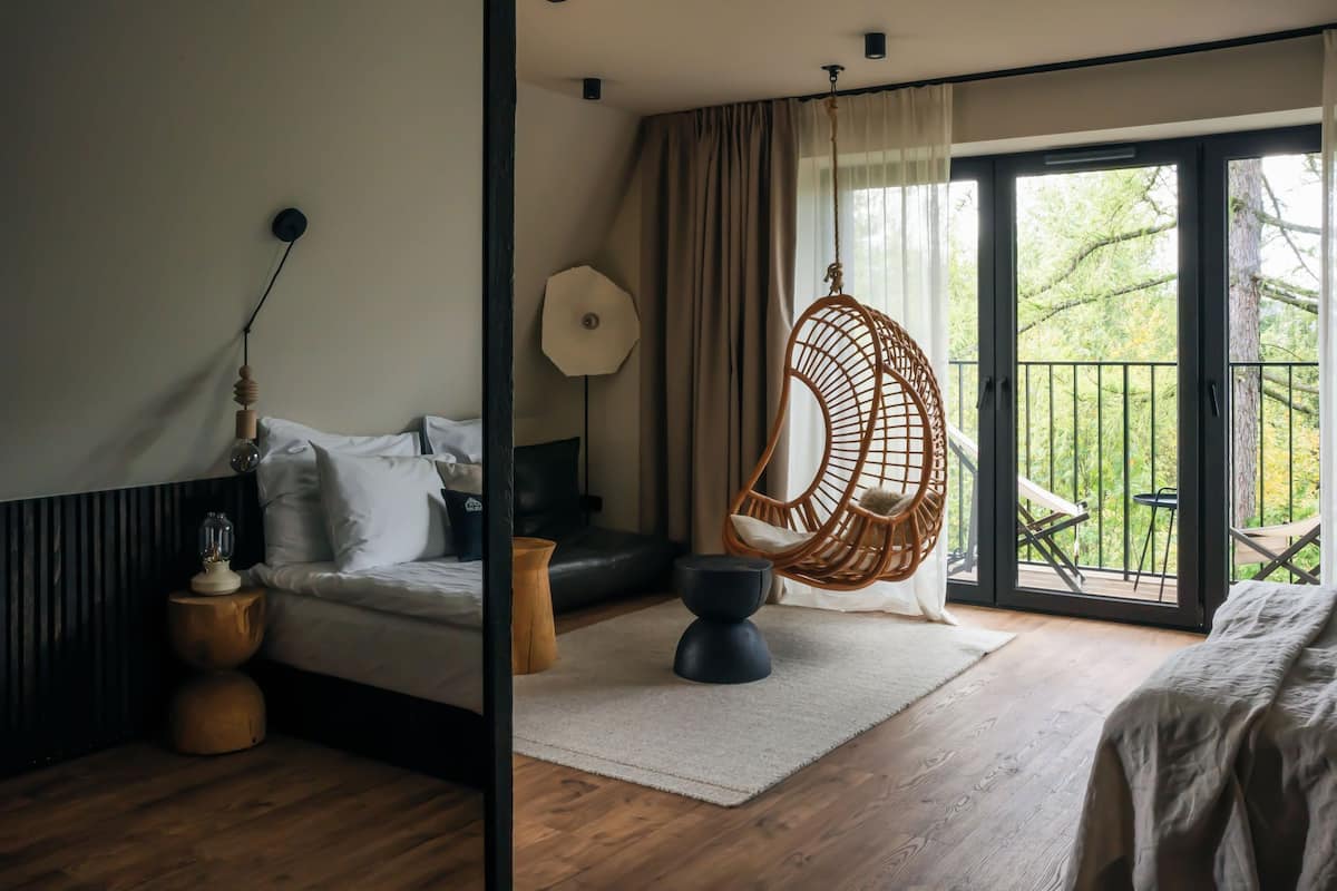 A bedroom with a bed, a hanging chair, a lamp, and a view of the outdoors.