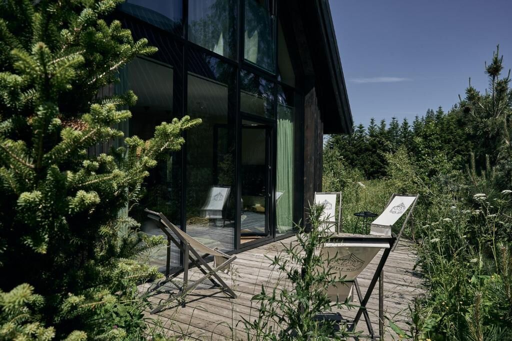 A modern building with large glass windows, a wooden deck, and outdoor seating.