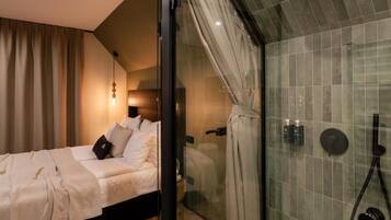 A modern bedroom with a glass shower enclosure, a bed with white linens, and a visible bathroom with a shower head and control panel.