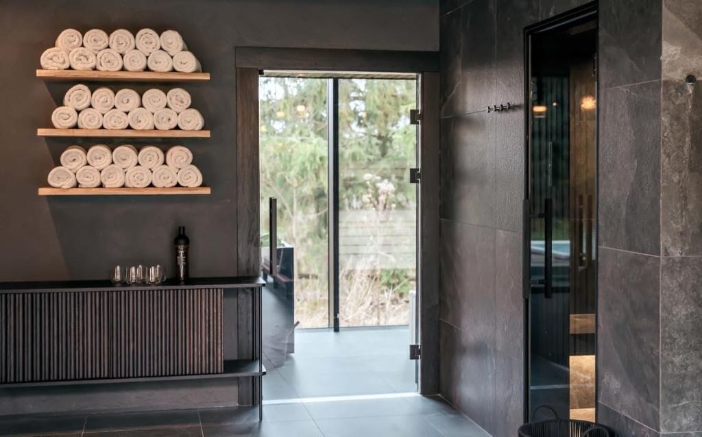 Un'area reception moderna con ripiani in legno che espongono asciugamani arrotolati, una scrivania della reception e una porta vetrata che dà sull'esterno.