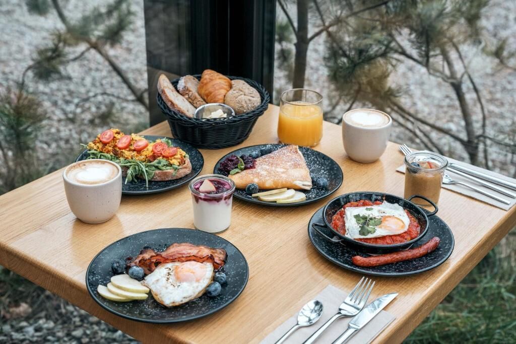 A breakfast table with various dishes, a basket of bread, and a glass of orange juice.