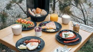 A breakfast table with various dishes, a basket of bread, and a glass of orange juice.