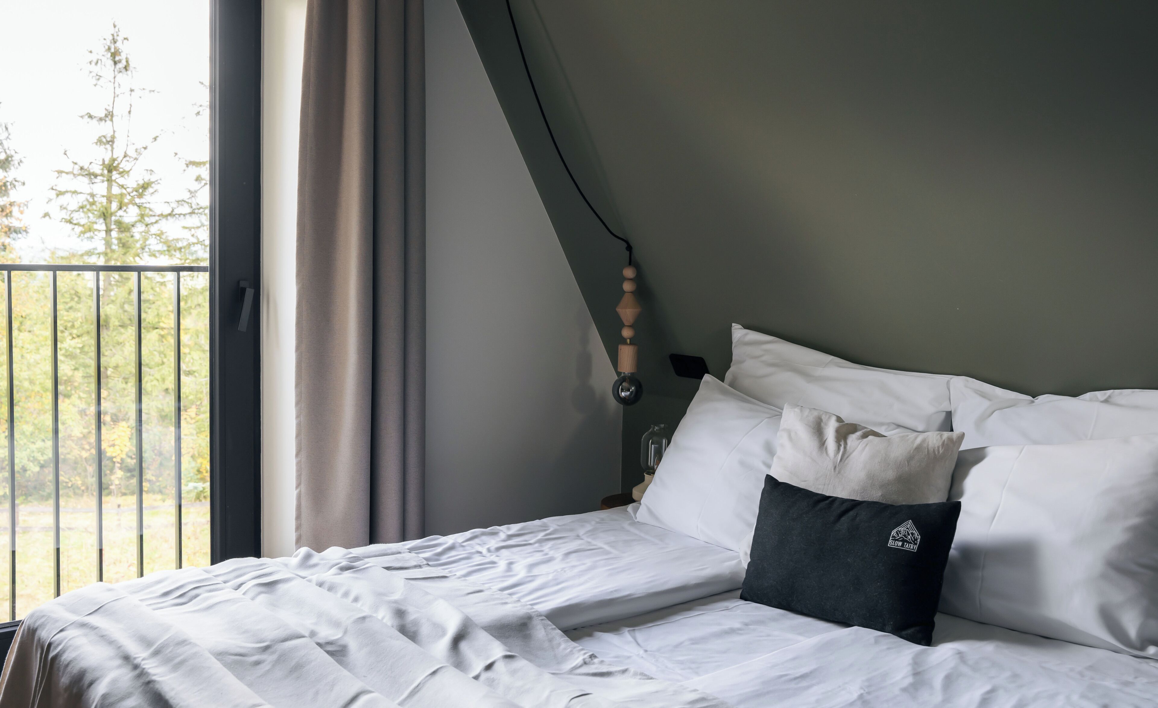 Un lit bien fait, avec des draps blancs, un oreiller foncé et une fenêtre avec des rideaux.